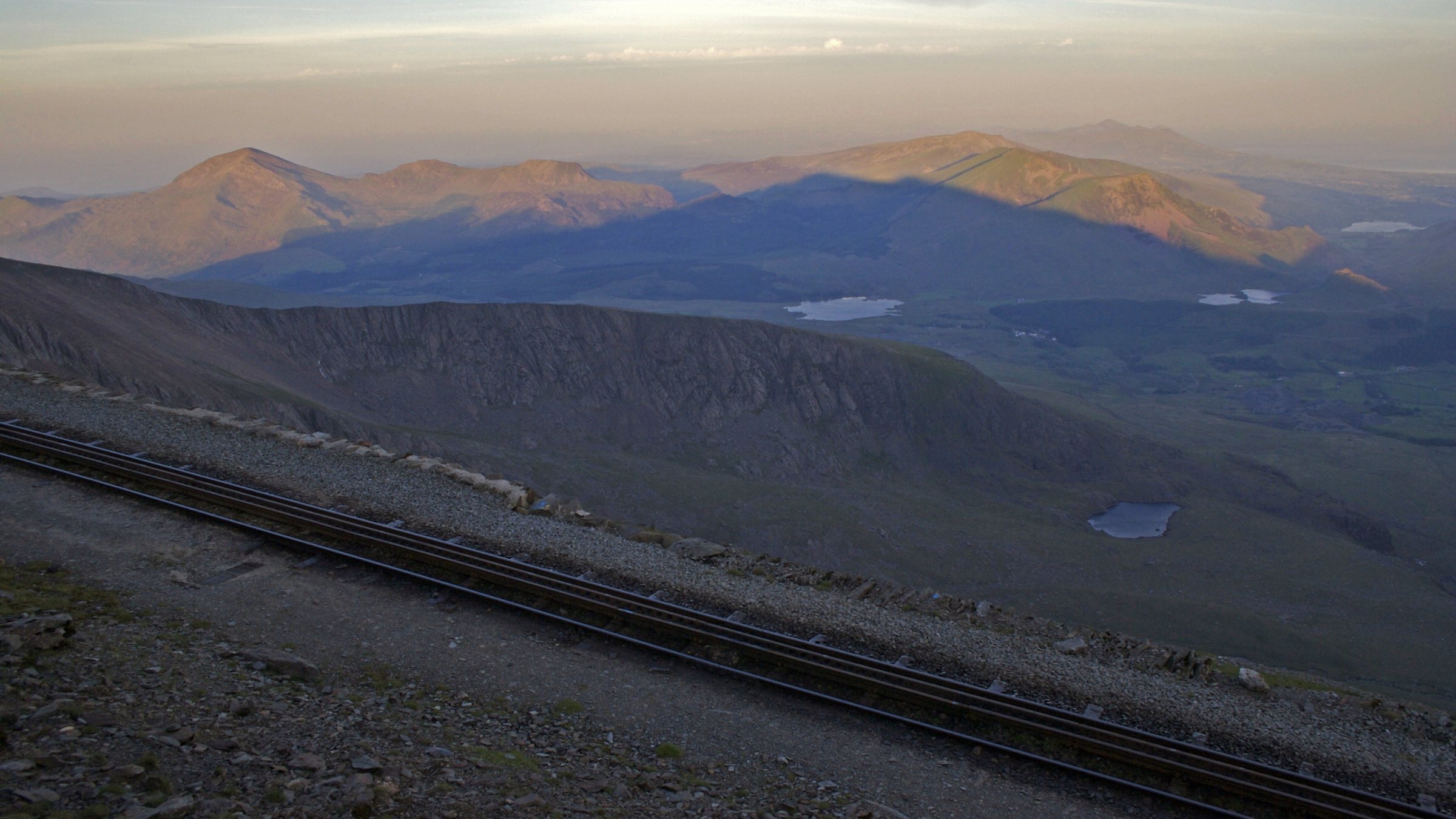 Sunrise from Yr Wyddfa, the mountain casting its own shadow across Eryri, with the Snowdon Mountain Railway track in the foreground